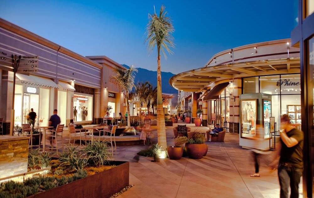 Open-air retail shopping center walkway at dusk with illuminated storefronts